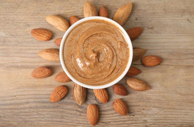 Delicious nut butter in bowl and almonds on wooden table, top view