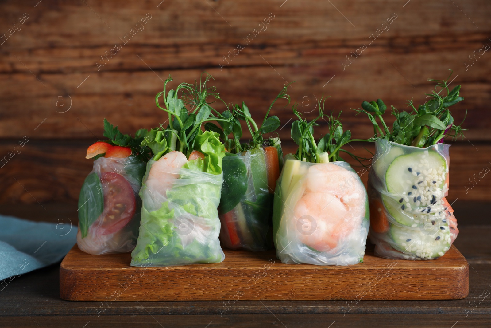 Photo of Many different delicious rolls wrapped in rice paper on wooden table