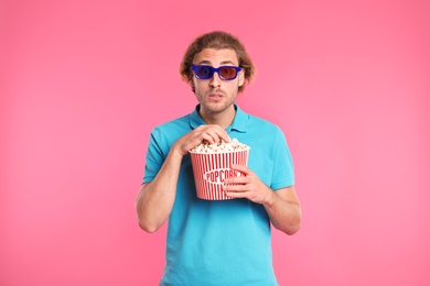 Emotional man with 3D glasses and popcorn during cinema show on color background