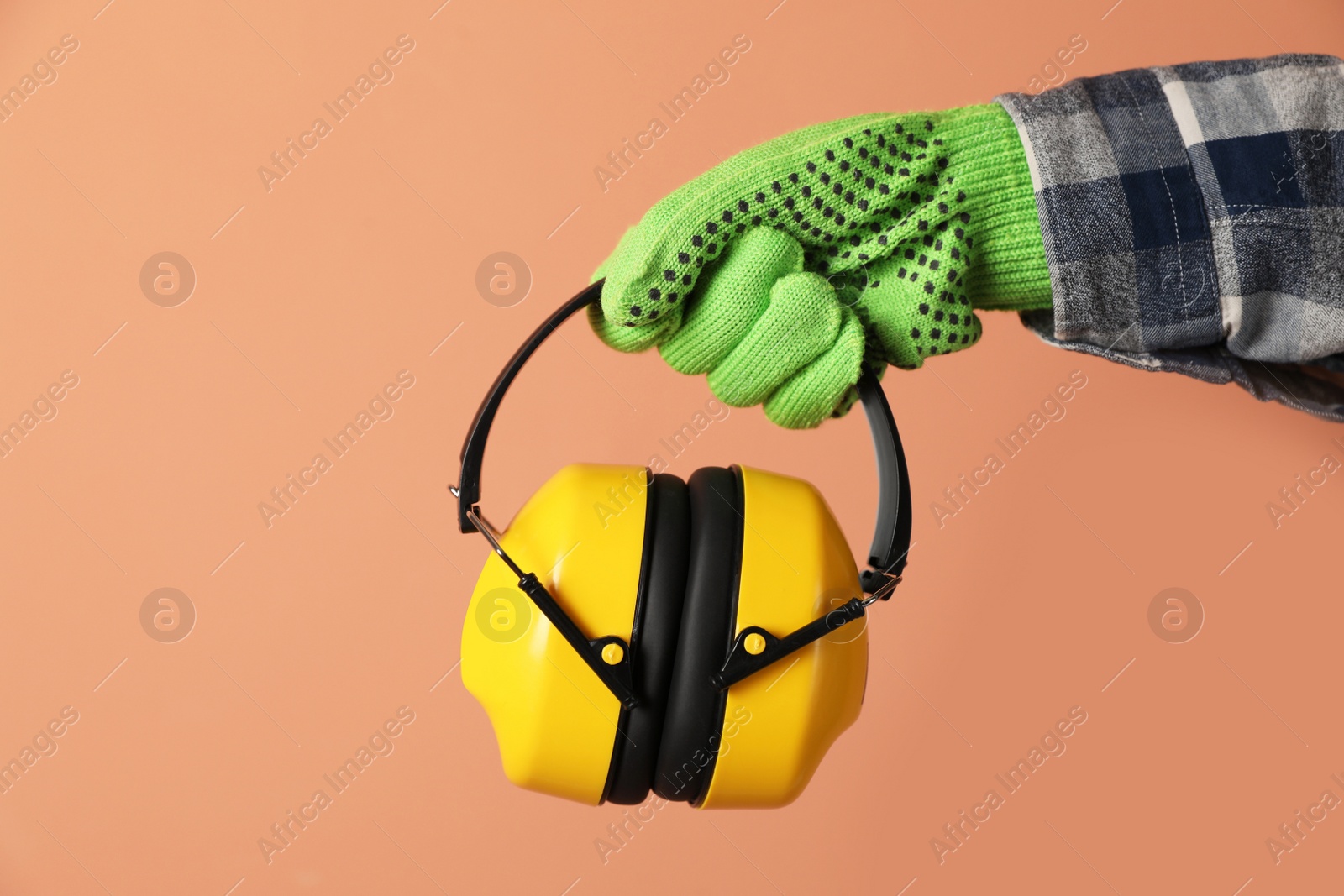 Photo of Worker holding safety headphones on coral background, closeup. Hearing protection device