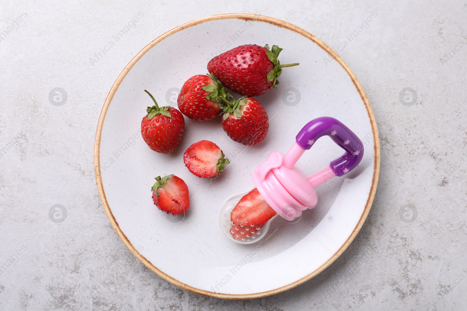 Photo of Nibbler with fresh strawberries on white table, top view. Baby feeder