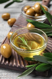 Photo of Bowl of cooking oil, olives and green leaves on wooden table