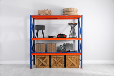 Photo of Metal shelving unit with wooden crates and different household stuff near light wall indoors