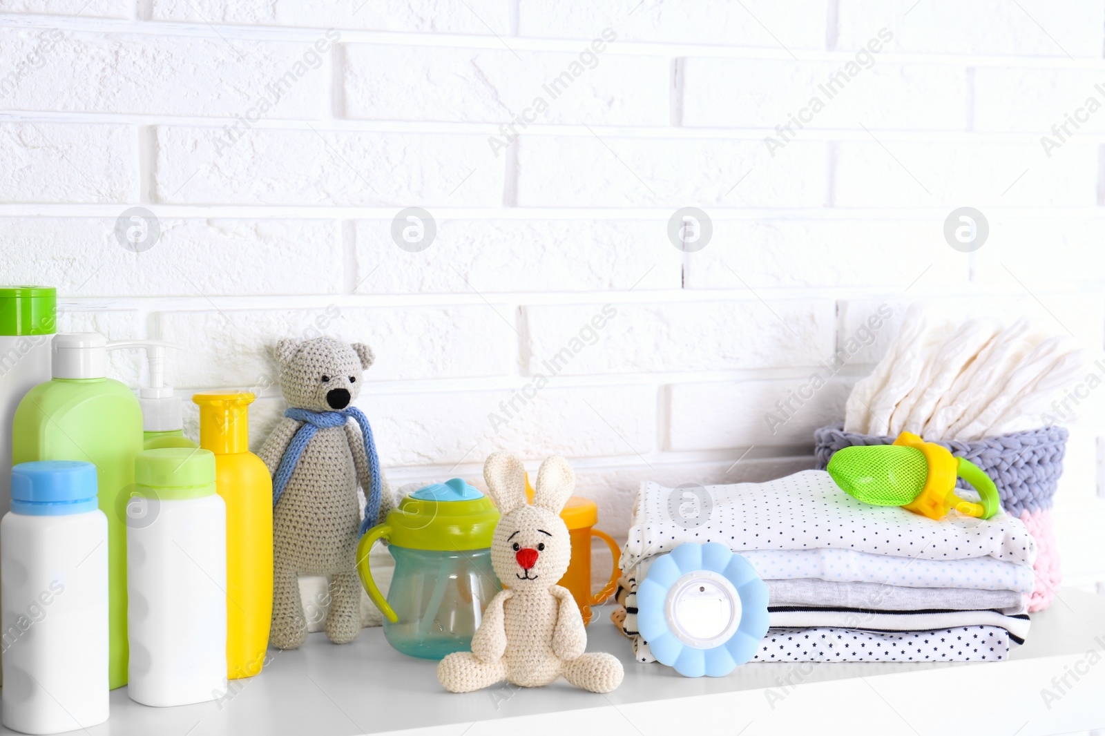 Photo of Baby accessories on shelf near white brick wall. Space for text