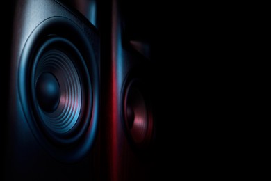 Photo of Modern sound speakers in neon light on black background, closeup. Space for text