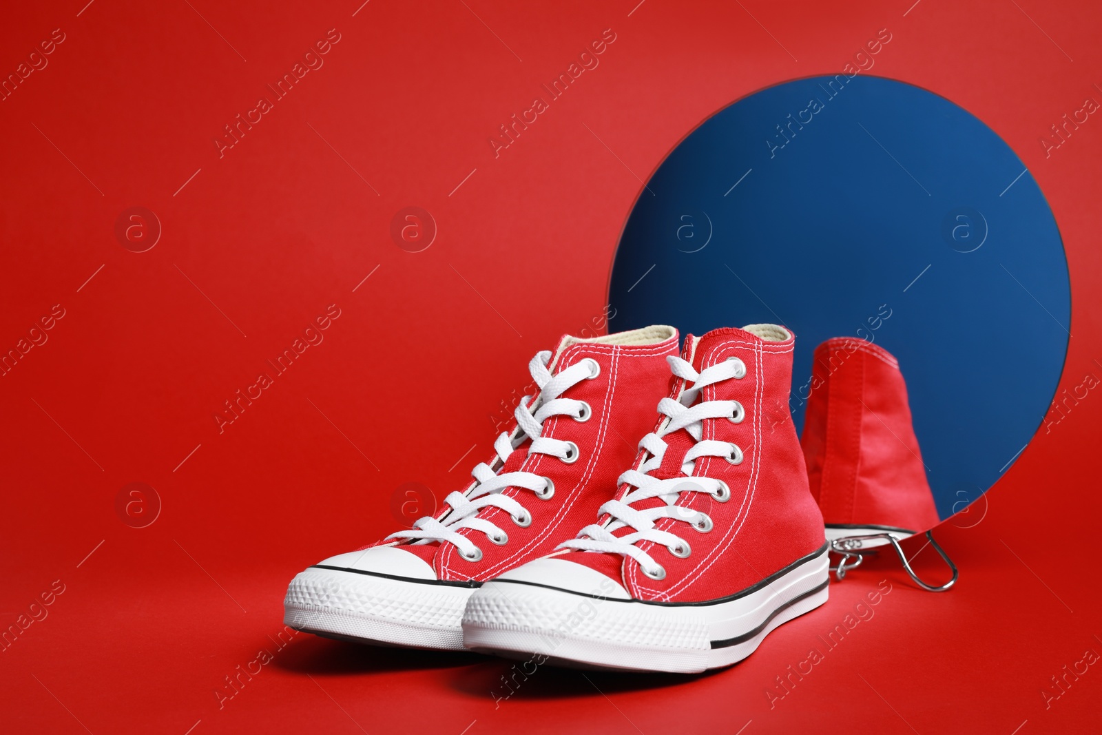 Photo of Pair of new stylish sneakers and mirror on red background