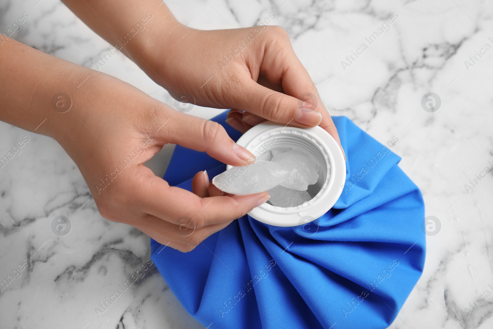 Photo of Woman putting ice cubes into pack at marble table, closeup