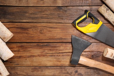 Photo of Saw with yellow handle, axe and firewood on wooden background, flat lay. Space for text