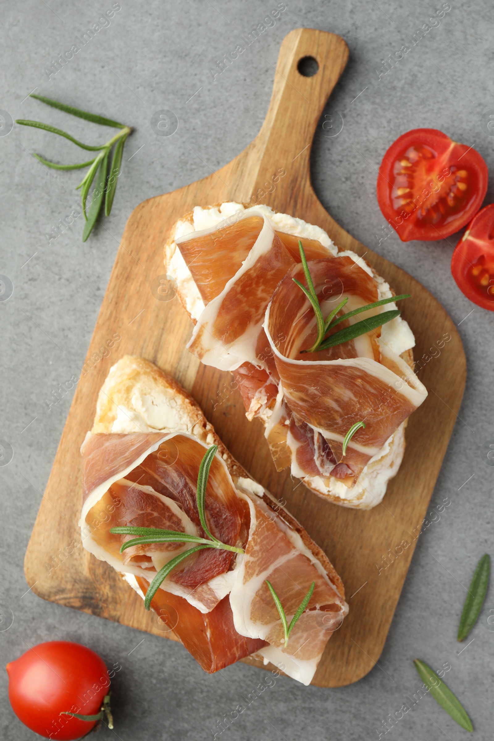 Photo of Tasty sandwiches with cured ham, rosemary and tomatoes on grey table, flat lay