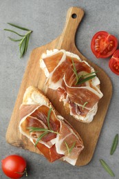 Tasty sandwiches with cured ham, rosemary and tomatoes on grey table, flat lay