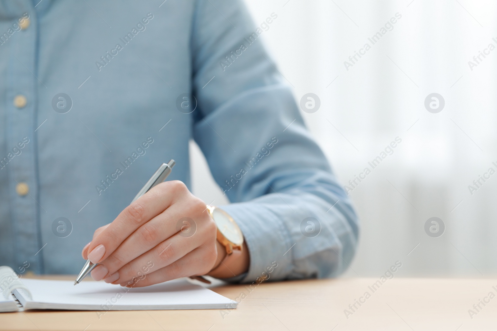 Photo of Woman writing in notebook at wooden table, closeup