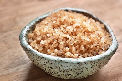 Photo of Bowl with brown sea salt on wooden table, closeup. Spa treatment