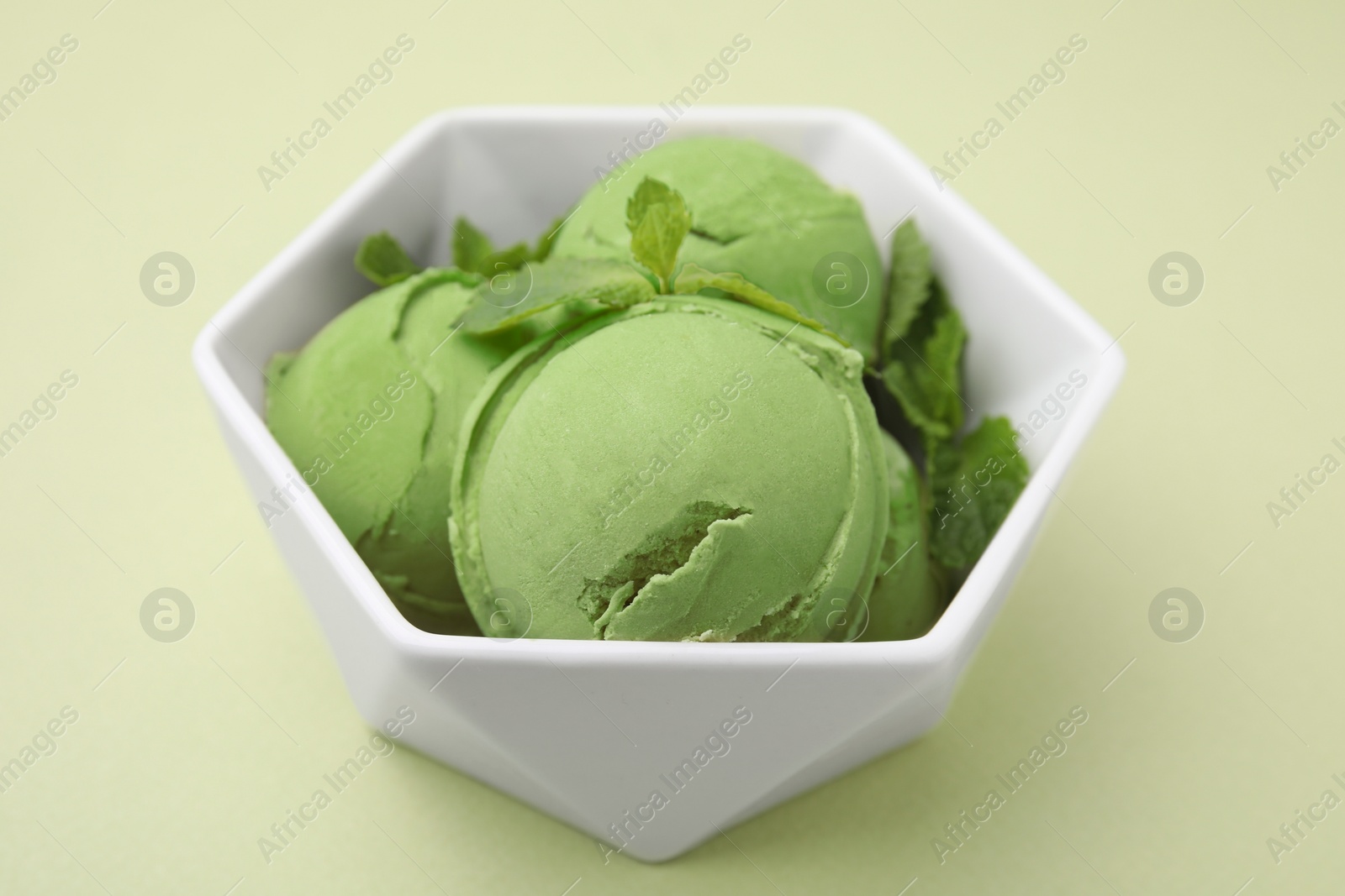 Photo of Tasty matcha ice cream with mint in bowl on pale green background, closeup