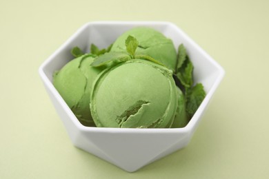 Tasty matcha ice cream with mint in bowl on pale green background, closeup
