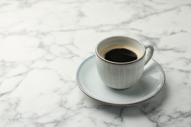 Photo of Tasty coffee in cup and saucer on white marble table, closeup. Space for text