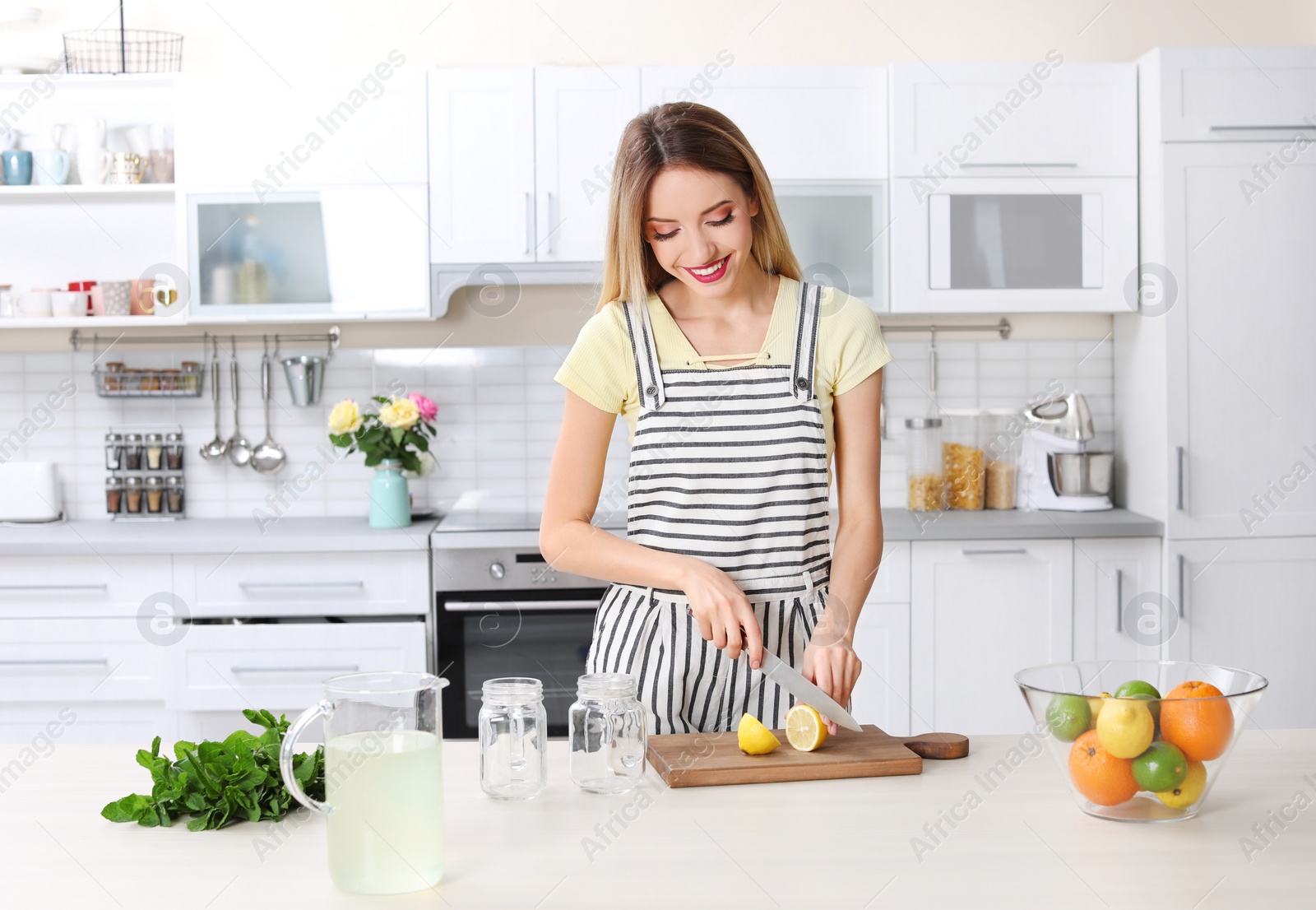 Photo of Young woman preparing lemonade on table in kitchen. Natural detox drink