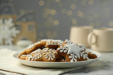 Photo of Tasty Christmas cookies with icing on white marble table against blurred lights, closeup