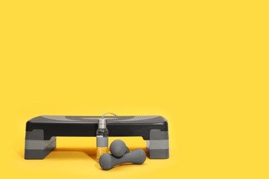 Photo of Step platform, dumbbells and bottle of water on yellow background, space for text. Sports equipment