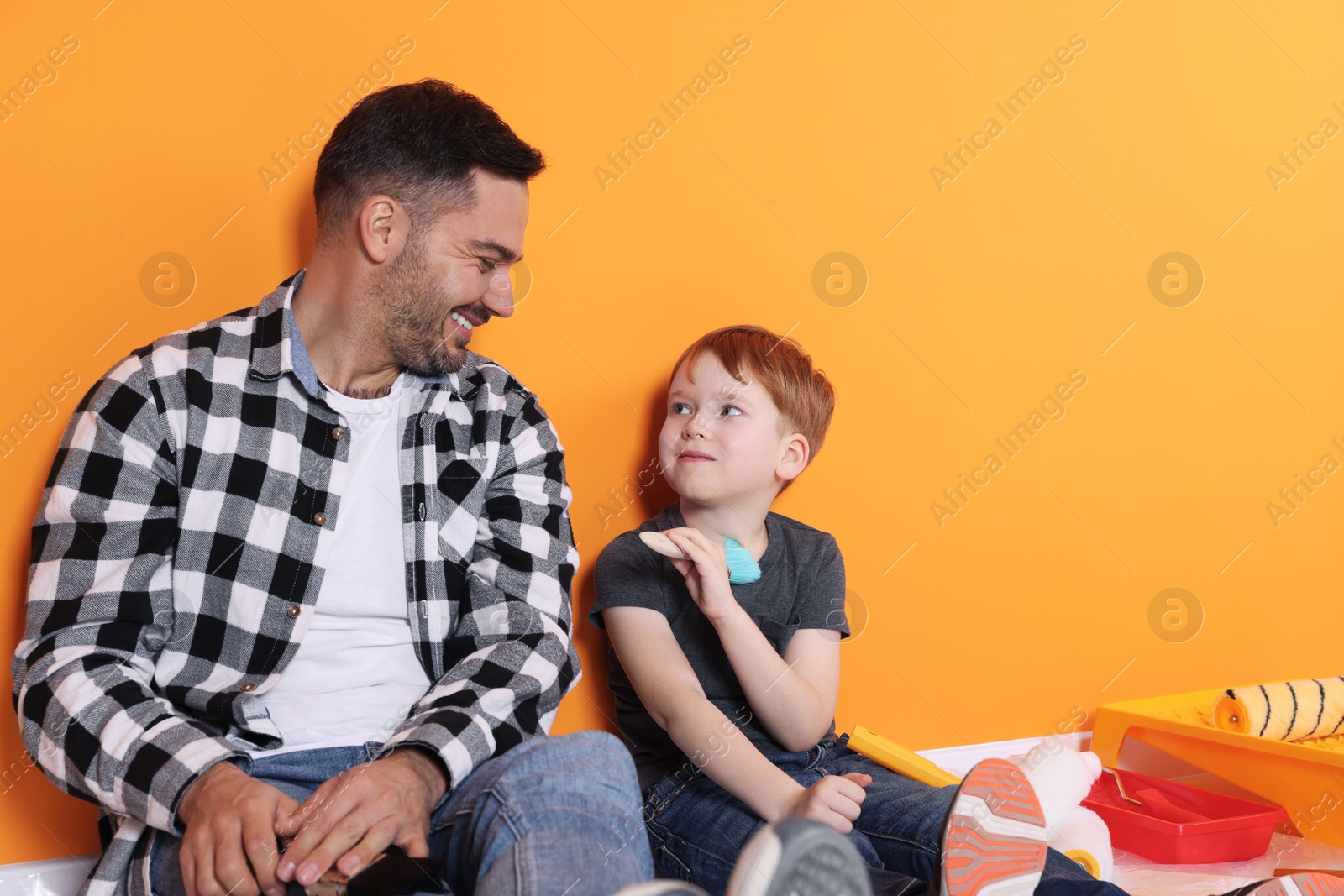 Photo of Father and son with repair tools near orange wall