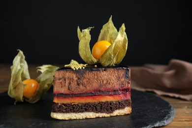 Piece of tasty cake decorated with physalis fruit on wooden table