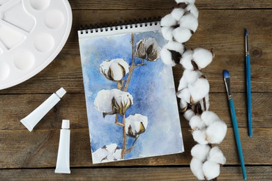Photo of Painting of cotton flowers in sketchbook and art supplies on wooden table, flat lay