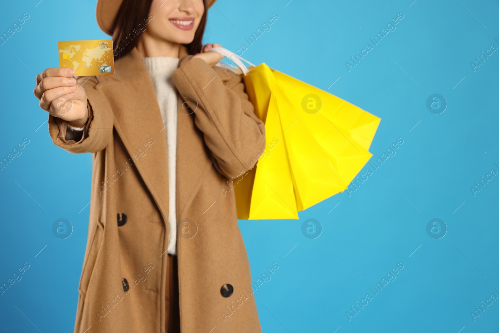 Photo of Woman holding shopping bags and credit card on light blue background, closeup