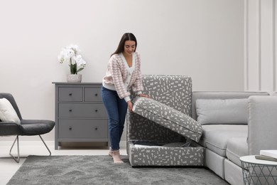 Photo of Woman closing modular sofa section with storage in living room