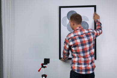 Photo of Man using cross line laser level for hanging painting on light wall, back view