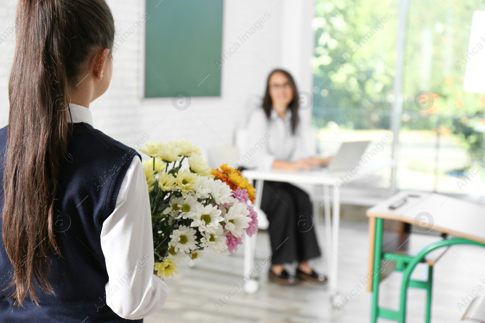 Photo of Schoolgirl with bouquet congratulating her pedagogue in classroom. Teacher's day