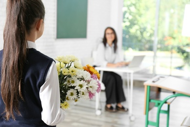 Photo of Schoolgirl with bouquet congratulating her pedagogue in classroom. Teacher's day