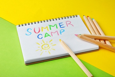 Notebook with written text SUMMER CAMP and different pencils on color background