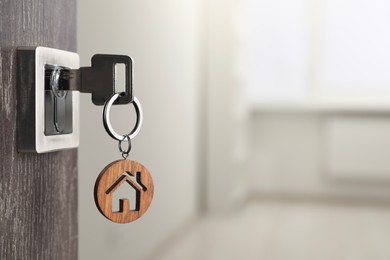 Photo of Mortgage and real estate. Open door with key and house shaped keychain against blurred background, space for text