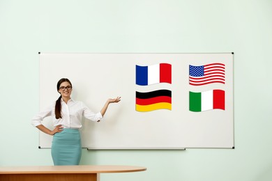 Image of Foreign languages teacher near whiteboard with different flags in modern classroom