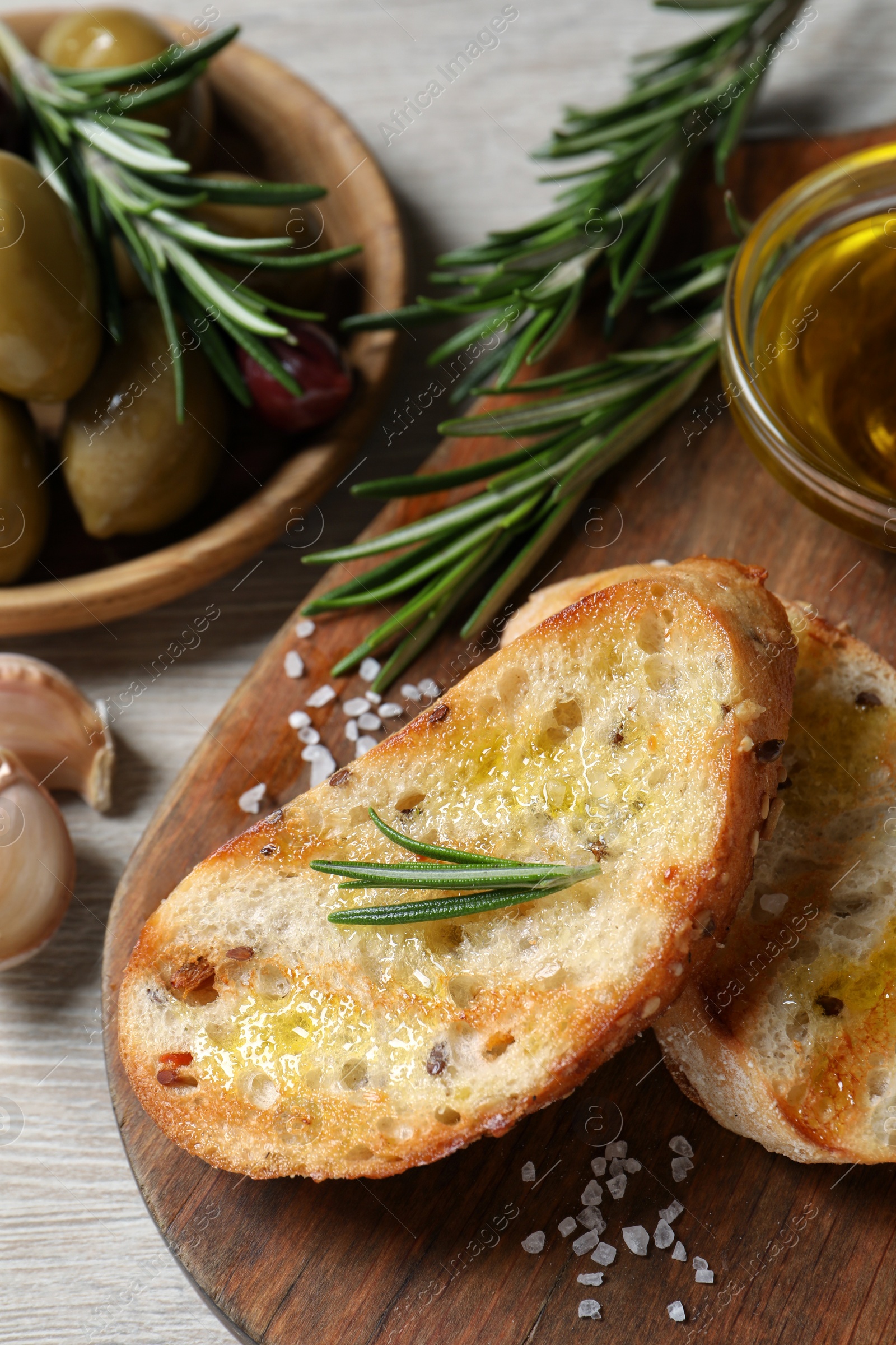 Photo of Tasty bruschettas with oil and rosemary on wooden board, closeup