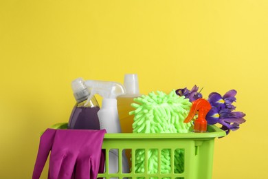 Spring cleaning. Basket with detergents, flowers and tools on yellow background, closeup