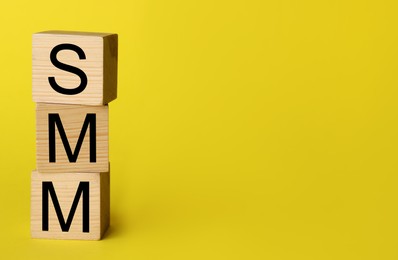 Wooden cubes with abbreviation SMM (Social media marketing) on yellow background. Space for text