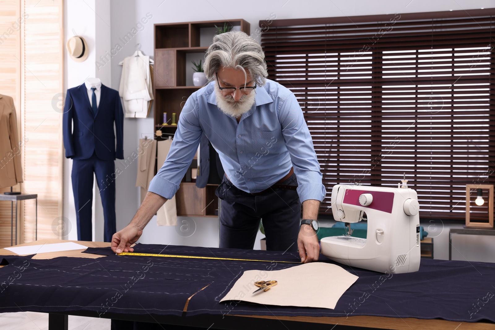 Photo of Professional tailor with measuring tape working at table in atelier