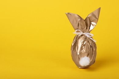 Easter bunny made of shiny gold paper and egg on yellow background. Space for text