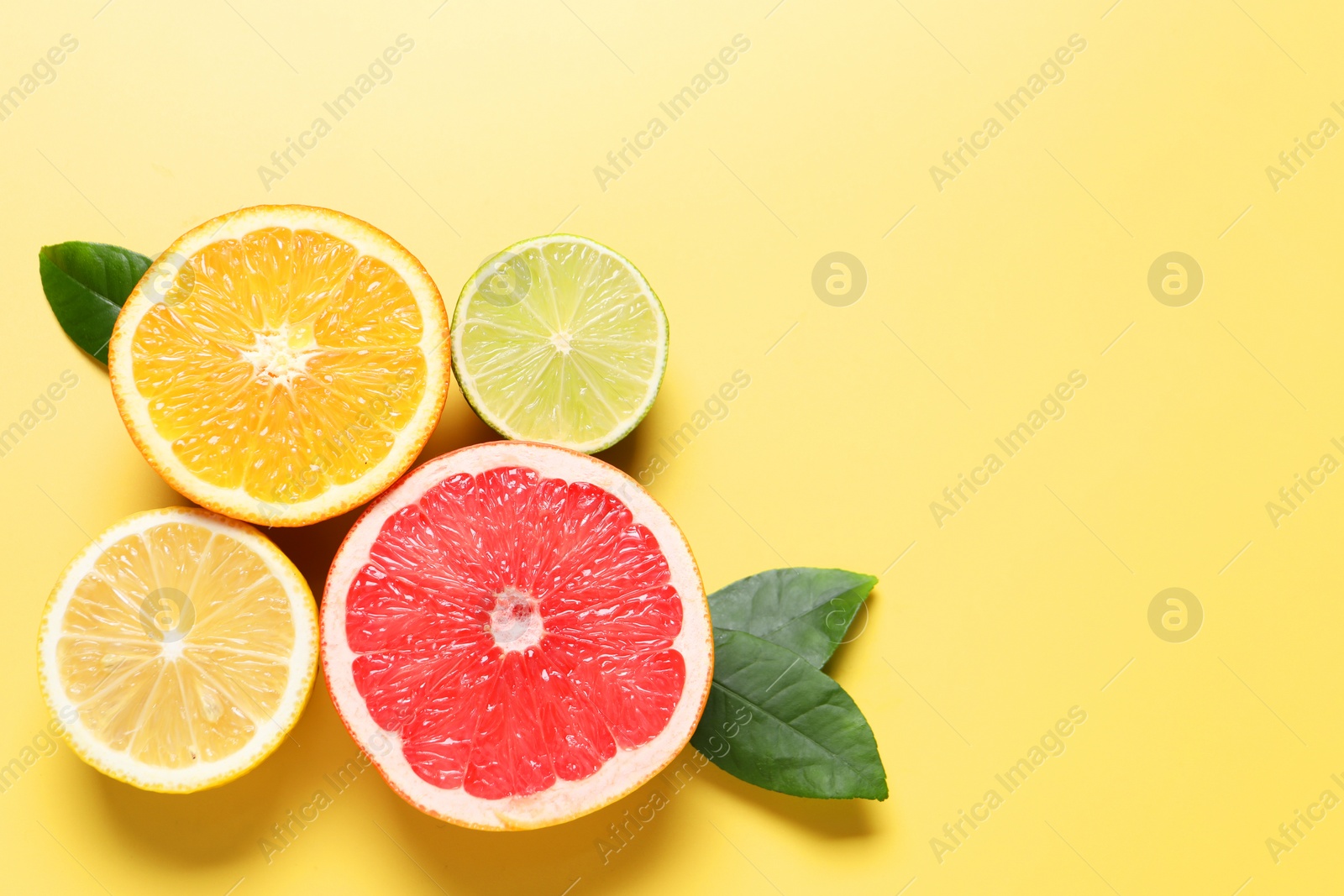 Photo of Different cut citrus fruits and leaves on yellow table, flat lay. Space for text