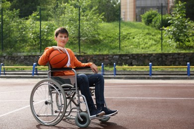 Photo of Disabled teenage boy in wheelchair with basketball ball at outdoor court