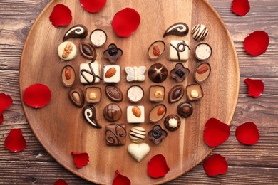 Photo of Heart made with delicious chocolate candies and rose petals on wooden table, top view