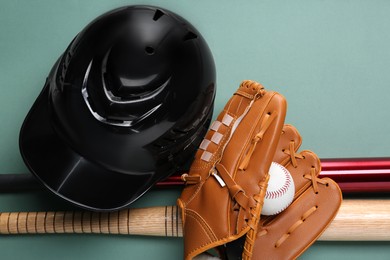 Baseball glove, bats, ball and batting helmet on pale green background, flat lay
