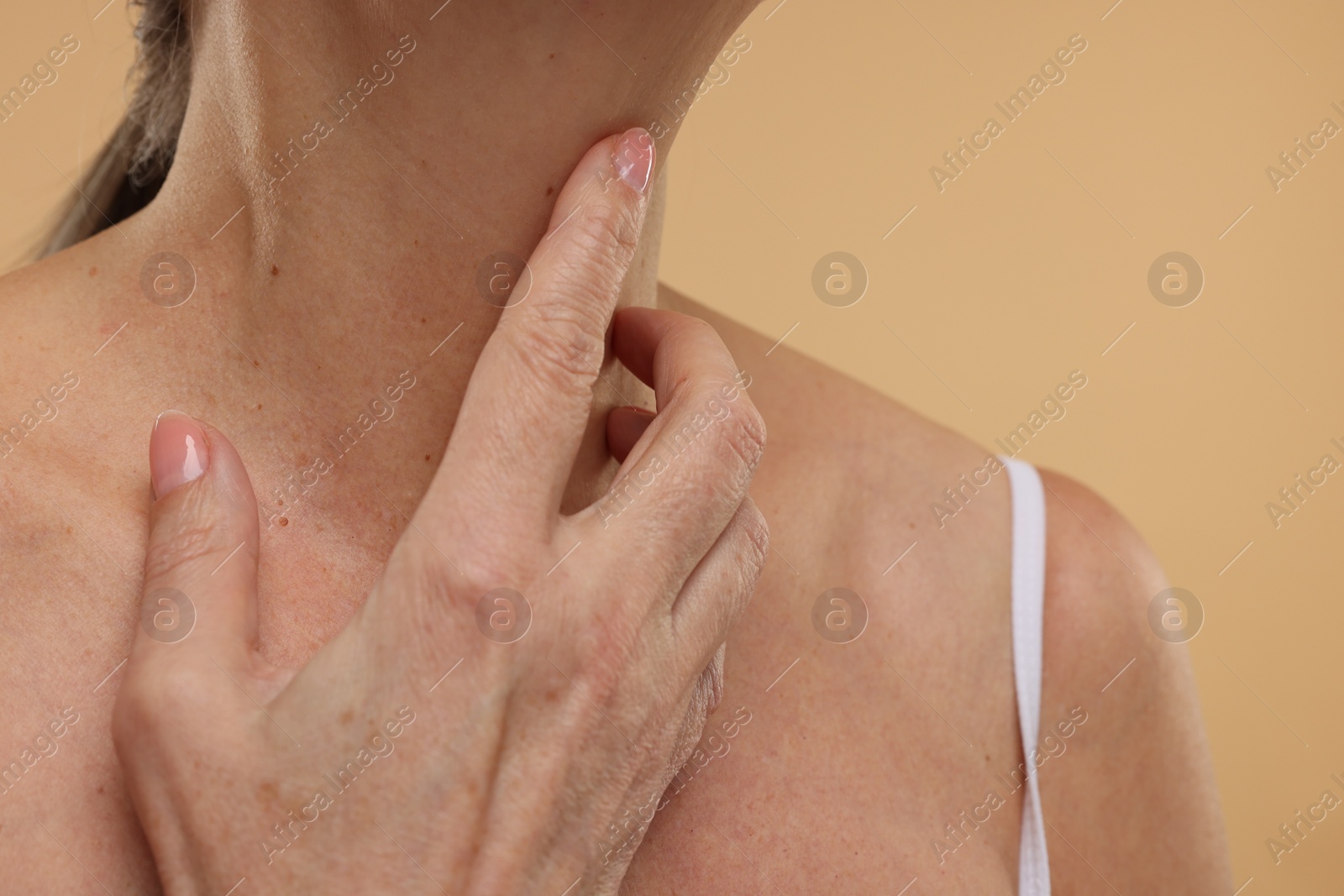 Photo of Mature woman touching her neck on beige background, closeup