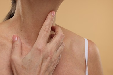 Mature woman touching her neck on beige background, closeup