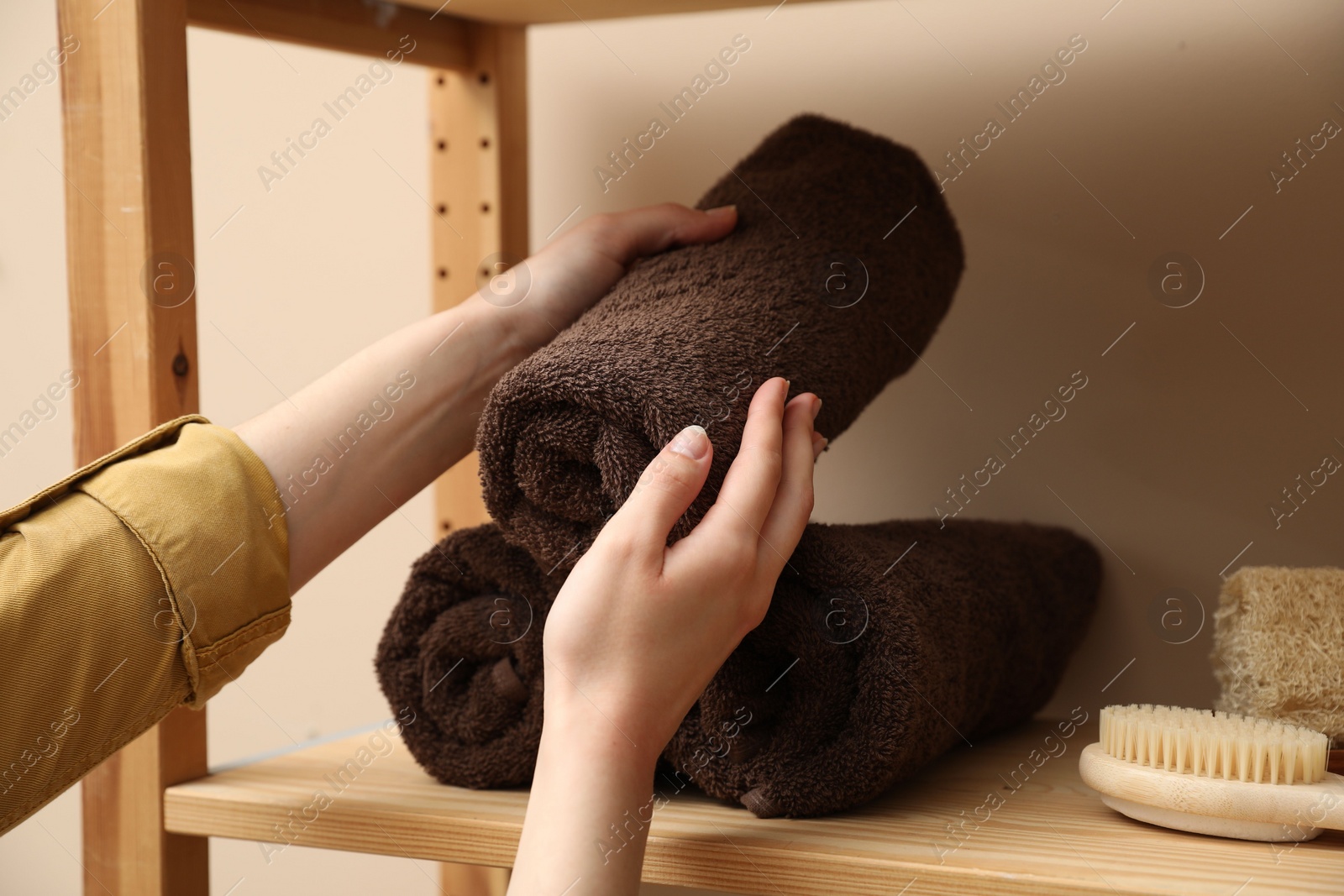 Photo of Woman taking rolled towel from shelf indoors, closeup