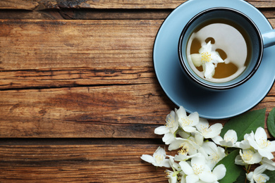 Photo of Cup of tea and fresh jasmine flowers on wooden table, flat lay. Space for text