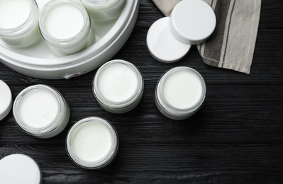 Photo of Modern yogurt maker and full jars on black wooden table, flat lay