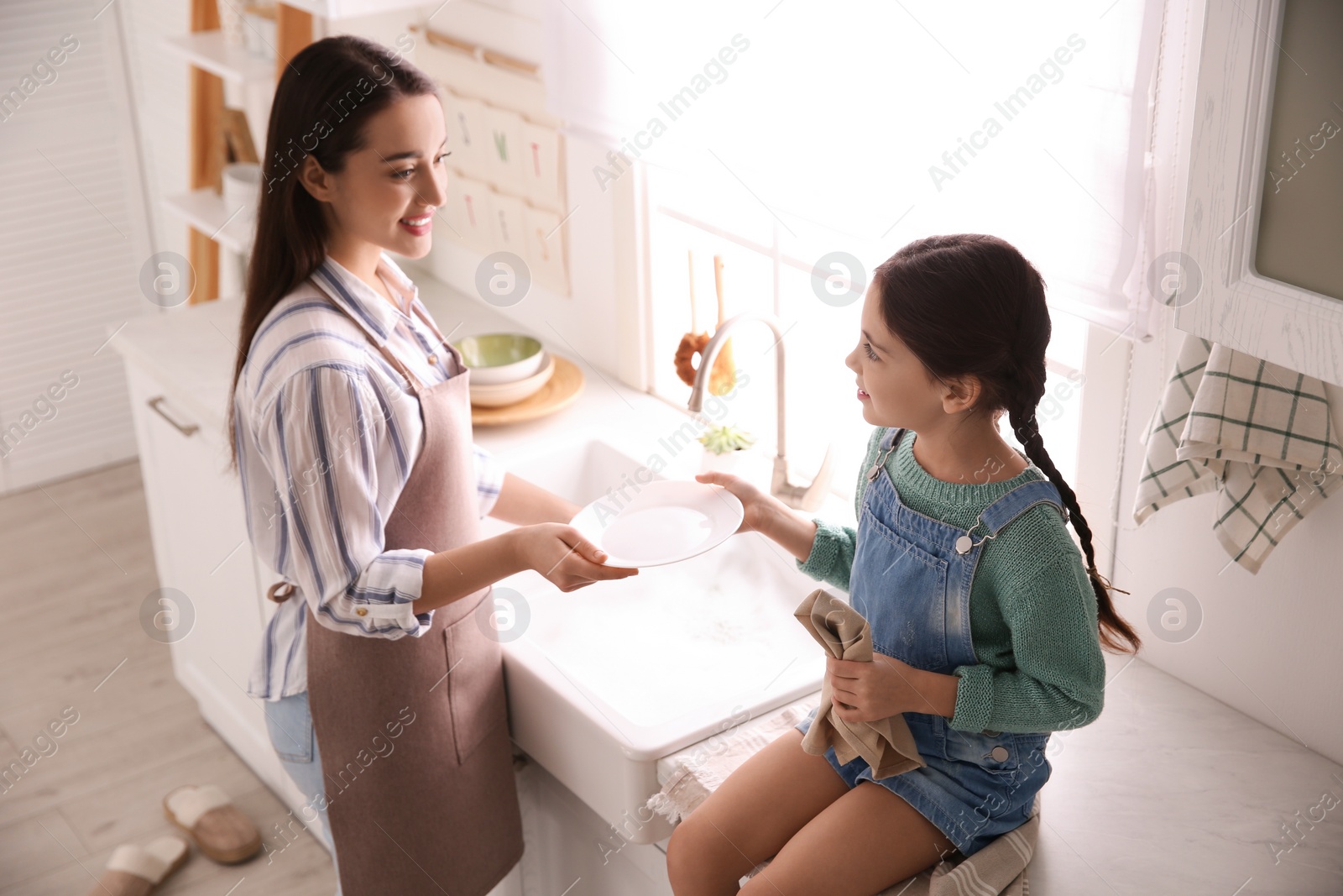 Photo of Mother and daughter washing dishes together in kitchen