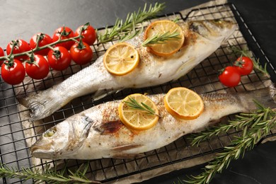 Photo of Baked fish with tomatoes, rosemary and lemon on black textured table, closeup