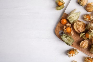 Ripe physalis fruits with dry husk on white wooden table, flat lay. Space for text